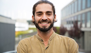 Bearded man outside smiling with buildings in background