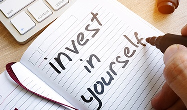 notebook with a person writing “invest in yourself” in it with a black marker