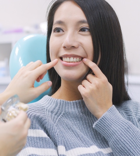 Woman in sweater sitting in dental chair and pointing to smile