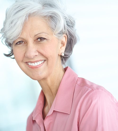 Woman in pink blouse showing off new dentures