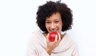 Woman with dental implants in Carrollton holding an apple