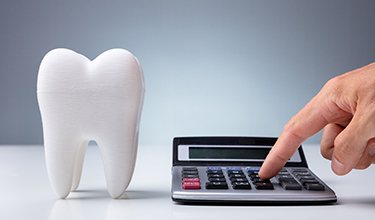 Model tooth and calculator symbolizing the cost of dental implants