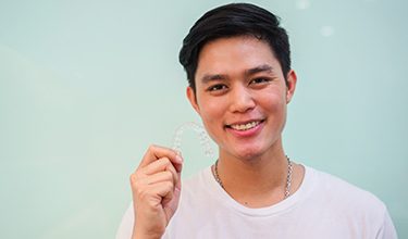 Younger man holding Invisalign clear aligner