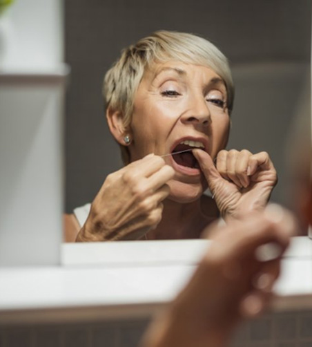 Woman flossing her teeth in bathroom mirror
