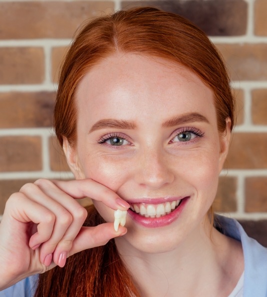 Red haired woman standing in front of brick wall and holding tooth