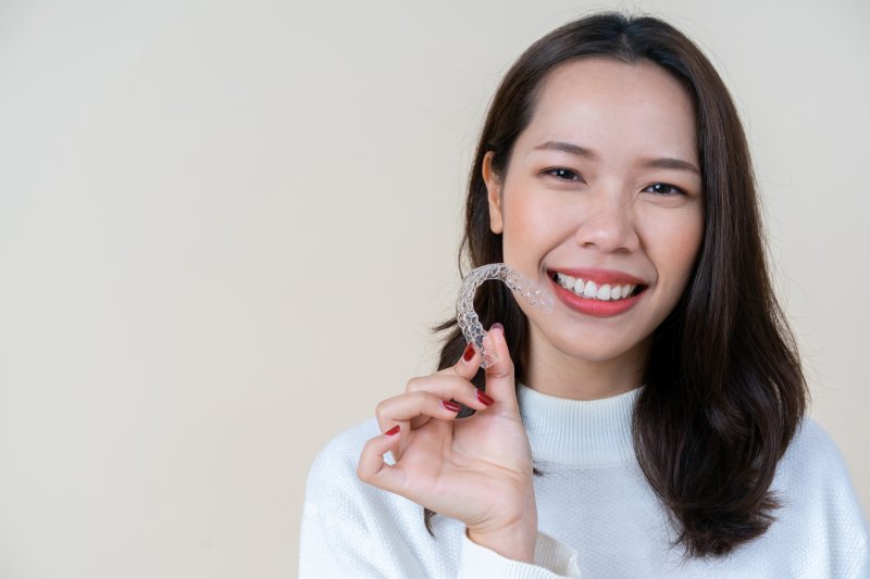 person holding up Invisalign retainer and smiling