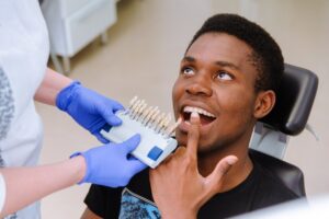 Patient pointing to tooth while doctor holds veneers up to his mouth. 